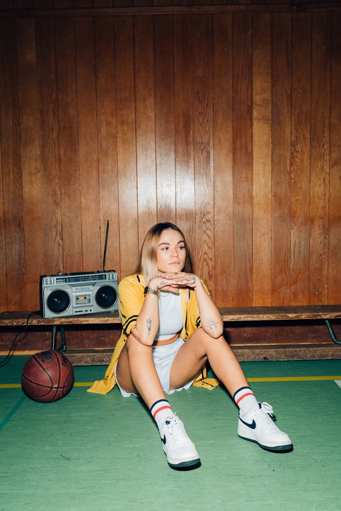 Portrait of a young woman in a gym, sitting with a basketball and vintage boombox.